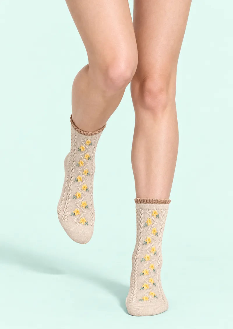 Top view of beige Crew Socks with yellow floral accents, green leaves, openwork knit and a ruffled cuff.