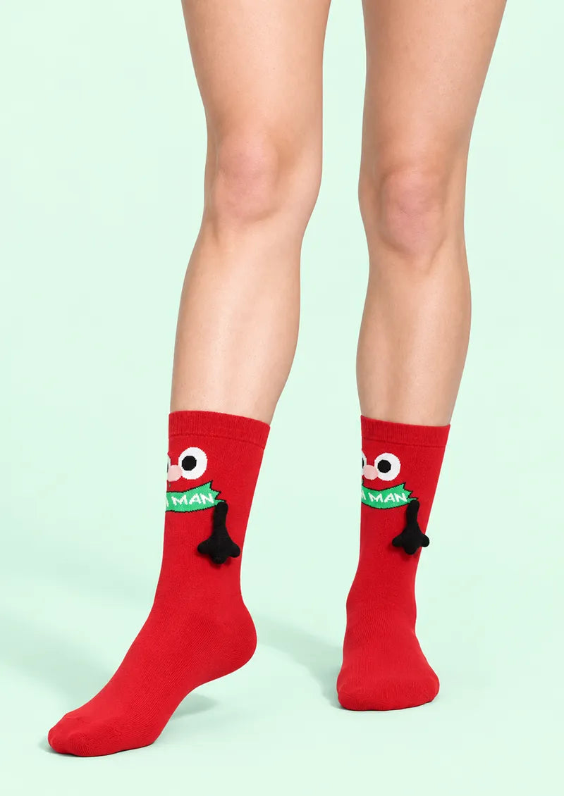 Front view of red Crew Socks with a cartoon Christmas character, green scarf detail, and black 3D accent