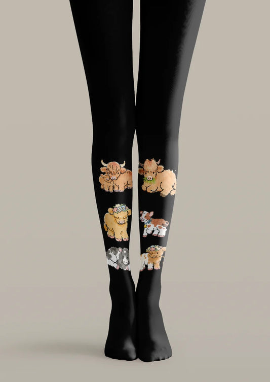 Black printed tights with brown Highland cows, flower crowns, and smaller white-marked calves arranged along the lower legs.