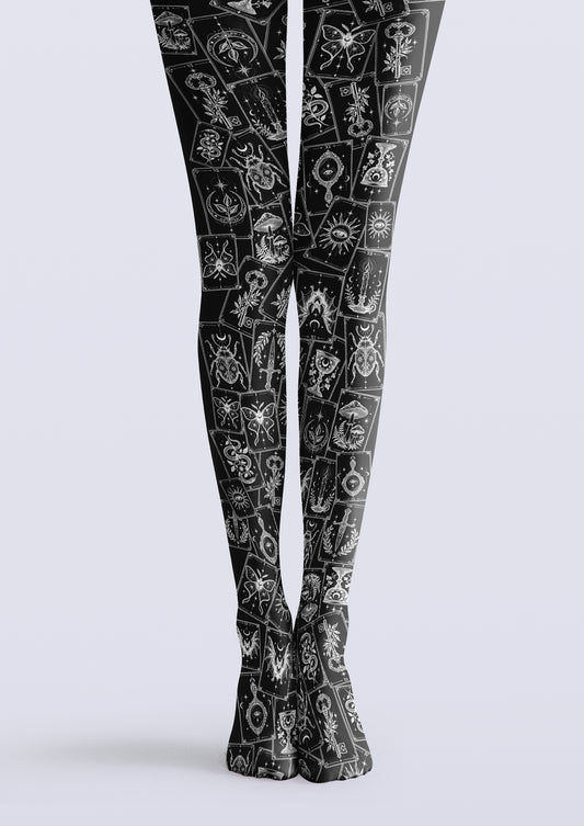 Black printed tights with overlapping cards in white linework, including moths, keys, suns, and crescent moons